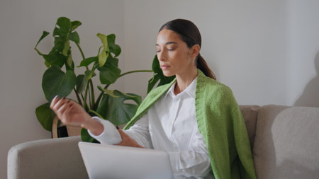Relaxed woman sipping tea resting cozy couch close up. Serious lady working laptop looking distance at home office. Young student girl drinking hot beverage studying online at plants interior flatの写真素材