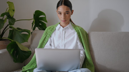 Freelance girl using laptop posing camera at flat portrait. Young smiling woman looking straight sitting sofa closeup. Relaxed freelancer lady resting couch holding computer at light apartment zoom onの写真素材