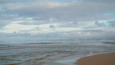 Sea waves hitting beach under cloudy sky. Peaceful ocean coastline with rippling waving water. Empty sandy shore on gloomy day. Tranquil solitude moment. Beautiful destination for outdoors relaxation.の写真素材