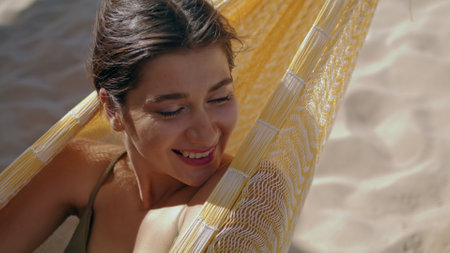 Woman chilling hammock beach alone portrait. Smiling beautiful girl closing eyes relaxing in bikini summer sunlight. Serene attractive lady dreaming looking camera at seashore. Seaside lounge concept.の写真素材