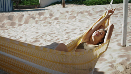 Relaxed girl sunbathing hammock on sandy beach. Beautiful carefree woman resting looking camera on summer vacation. Happy dreaming tourist lying enjoying sunlight. Weekend leisure at seashore concept.の写真素材