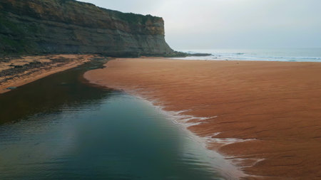 Panoramic marine beach landscape at cloudy day. Serene sandy coast calm ocean waves slow motion. Grey sea water surface washing seaside with volcanic cliffs background. Stormy wild scenery conceptの写真素材