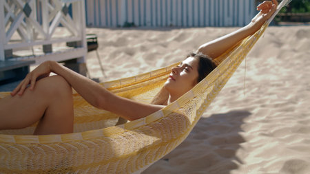 Happy girl lying hammock closeup. Attractive smiling woman enjoying sunlight relaxing at beach house. Beautiful lady closing eyes dreaming on idyllic seashore vacation. Lounge carefree mood concept.の写真素材