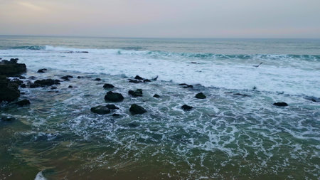 Cloudy ocean splashing cliffside nature at beach closeup. Big waves covering volcanic rocks at remote shore slow motion. Foamy water breaking coast of exotic island seabirds flying. Marine conceptの写真素材
