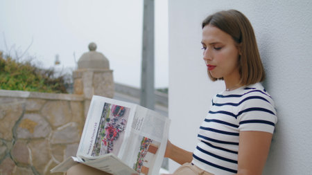 Focused girl reading newspaper outdoors closeup. Beautiful tourist relaxing checking local magazine in morning. Carefree woman resting on terrace enjoying vacation alone. Peaceful weekend concept.の写真素材