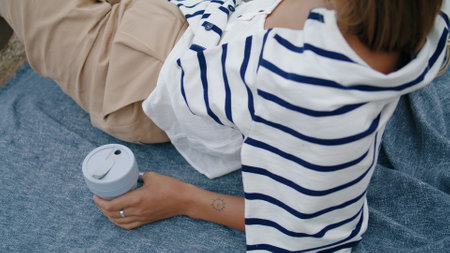 Hand holding reusable coffee cup closeup. Serene girl drinking morning beverage resting on ocean...