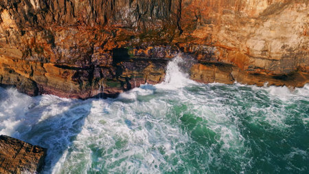 Amazing sea waves breaking on coastal rocks slow motion. Powerful stormy ocean water splashing washing seaside cliffs making white foam sunny day. Aerial view marine landscape dangerous seashore.の写真素材