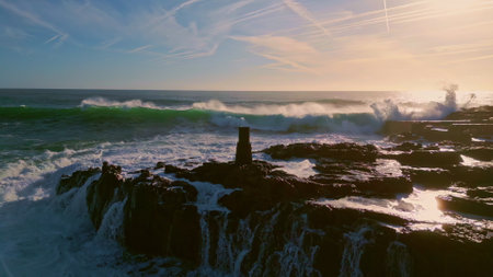 Foaming sea water breaking on dark stones super slow motion. Aerial view stormy rough ocean crashing coastal rocks making white foam. Amazing nature landscape dangerous rocky coast at bright sunny dayの写真素材