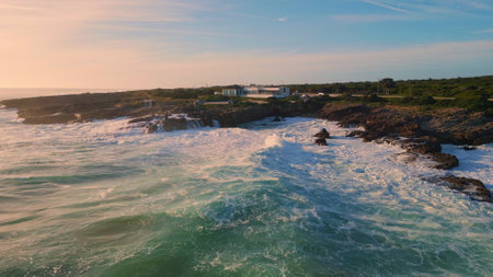 Aerial view stony coastline washing by beautiful stormy ocean in slow motion. Powerful sea waves rolling rocky seashore making white foam. Sunny marine landscape splashing dangerous coastal cliffsの写真素材