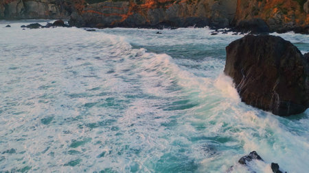 Foamy waves rolling stone shoreline closeup. Picturesque drone view stormy sea water washing empty rocky coast super slow motion. Cinematic marine panorama ocean swell running on volcanic beachの写真素材