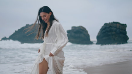 Carefree happy woman running at ocean waves on evening dusk. Smiling attractive girl jumping on sand coast wearing white dress. Cheerful lady tourist enjoy freedom happiness on vacation at seashore.の写真素材
