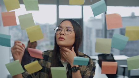 Thoughtful freelancer pondering sticker wall office closeup. Young businesswoman writing tasks on...