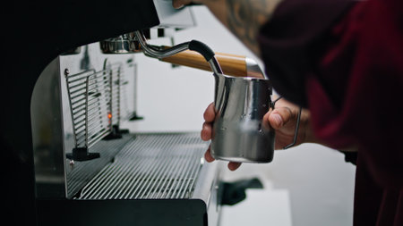 Barista hands preparing latte on professional coffee machine close up. Unknown tattooed man whipping milk foam for delicious latte. Young bartender making tasty espresso using modern cafe machine.の写真素材