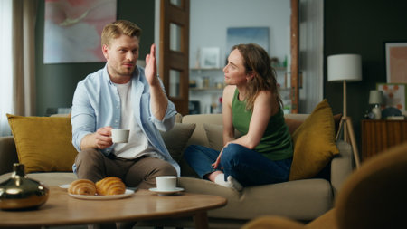 Chilling spouses drinking tea at sofa interior. Love couple enjoying coffee cups talking together at apartment. Smiling husband wife sipping hot beverage relaxing couch. People home lifestyle conceptの写真素材