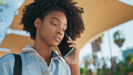 Sad girl talking cellphone walking sunny street close up. Portrait of attractive african american teenager dissatisfied phone call outdoors. Curly nervous young lady speaking smartphone on stroll.の写真素材