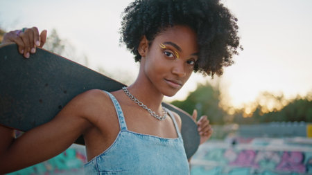 Girl hipster holding skate board looking camera with cheeky smile closeup. Beautiful african...