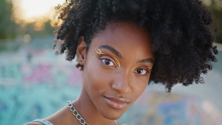 Portrait of funky teen model looking camera with smile outdoors. Gorgeous trendy girl with modern makeup posing at evening street alone. Cute african american female model smiling having fun close up.の写真素材