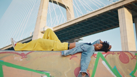 Black haired girl lying city street in front urban bridge close up. Relaxed african american young...