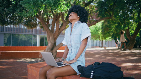 Tired woman working laptop sitting beautiful green park. Frustrated african american girl freelancer stretching painful neck looking notebook screen. Fatigued teenager dissatisfied remote internet jobの写真素材