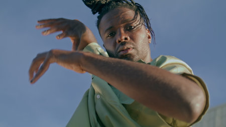 Modern dancer looking camera sky background portrait. Freestyle man making contemporary dance improvisation at open air closeup. African american guy moving hands slow motion. Youth culture conceptの写真素材