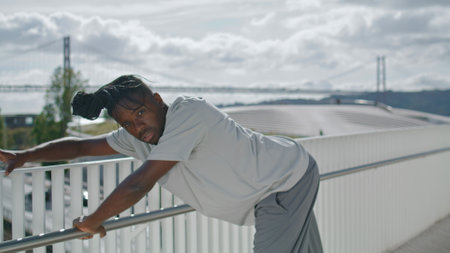 Acrobatic performer rehearsing dance at sea background. Dramatic man showing real emotions alone. African american dancer improvisation on metal bridge. Talented artist dancing creative city freestyleの写真素材