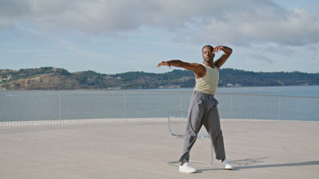 Plastic guy moving embankment dynamically closeup. Athletic african american person performed artistic dance moves. Flexible man dancing sea background. Ballet dancer showing contemp style techniquesの写真素材
