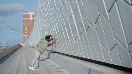 Artistic man dancing stadium alone closeup. Brown skin dancer touching concrete wall looking camera in modern district. African american professional showing different contemporary techniques at cityの写真素材