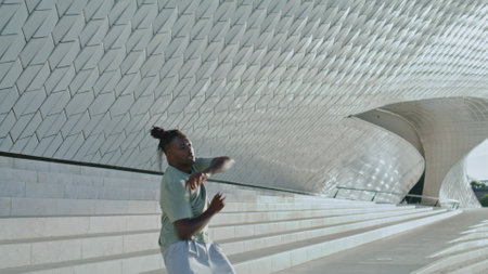 Inspired guy breakdancing stairs wide shot. African american man performing contemporary dance moves alone. Sportive dancer practicing freestyle at city wall background. Professional hip hop conceptの写真素材