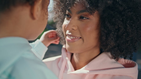 Mother smiling looking on child at family weekend outdoors close up. Portrait of cheerful african american woman at watching little girl with love tenderness. Carefree couple enjoying time together.の写真素材