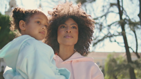 African american mother carrying daughter walking on sunny park close up. Attractive happy woman enjoying stroll with little girl on nature. Carefree family weekend together. Motherhood happiness.の写真素材