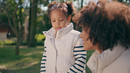 Cute girl feeding pigeons with happy mother at sunny green park close up. Little african american child throwing food to gray wild birds outdoors. Smiling mom looking at sweet daughter having fun.の写真素材