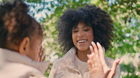 Happy woman playing with daughter on sunny nature closeup. Cheerful african american mother girl...