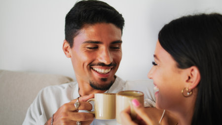 Young couple enjoying coffee on comfy couch closeup. Morning leisure time at home. Smiling spanish family talking drinking beverages together on weekend. Relaxed girl brunette man speaking laughingの写真素材
