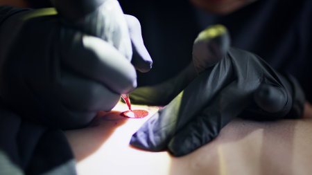 Artist hands tattooing red ink on skin closeup. Unrecognizable master wearing sterile gloves working professional machine at studio. Person fingers holding work equipment creating forms and linesの写真素材