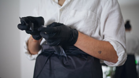 Woman hands wrapping tattoo machine at home. Unknown girl putting disinfectant coating at work gadget at studio closeup. Skilful artist fingers assembling equipment preparing to session at workplaceの写真素材