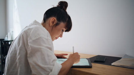 Serious lady working pad computer at remote office. Involved tattoo artist creating sketch at graphic tablet closeup. Artistic woman engaged in creativity at wooden desk workplace. Occupation conceptの写真素材