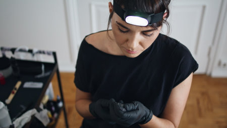 Tattoo artist assembling machine at salon closeup. Focused woman preparing to session sitting workplace. Involved tattooist holding work tool equipment in creative studio. Tattoo process conceptの写真素材