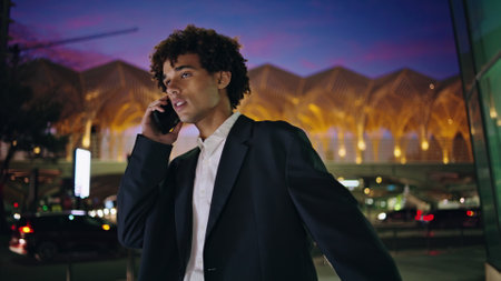 Calling man peeping taxi at night town closeup. Happy businessman waving hand meeting friend at dark downtown. Curly hair employee standing at bus stop waiting public transport at illuminated cityの写真素材