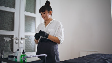 Thoughtful girl preparing workplace at home studio. Serious artist putting tattoo machine at work counter alone zoom on. Calm woman assembling equipment before tattooing session at domestic salonの写真素材