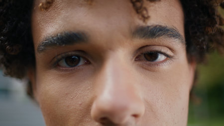 Brown eyes man looking camera outdoors extreme closeup. Curly hair teen staring lens attentively at street portrait. Handsome youngster clear sight detailed macro view. Focused human face expressionの写真素材