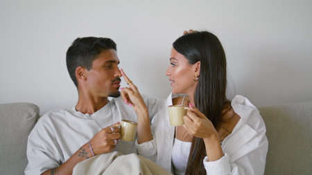 Cute newlyweds flirting lounge sofa closeup. Love happy couple holding espresso cups home. Sensual people hugging touching noses with tenderness indoor. Young family enjoying romantic date on couchの写真素材