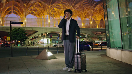 Young manager calling taxi at dark city. Travelling guy waving hand standing at urban glass airport background. Formal wear businessman moving to transport at night street. Business trip conceptの写真素材