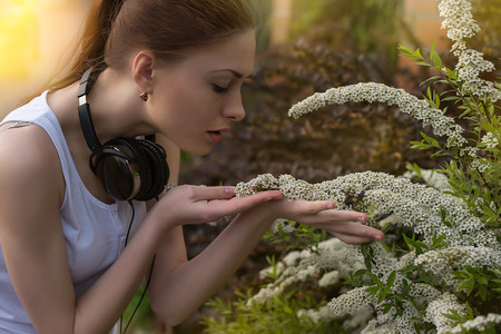 Beautiful young woman with headphones smelling white flowersの写真素材