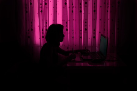 Silhouette of the girl at the computer in the purple roomの写真素材