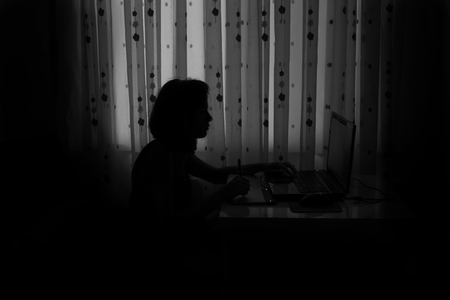 Silhouette of the girl at the computer in the roomの写真素材