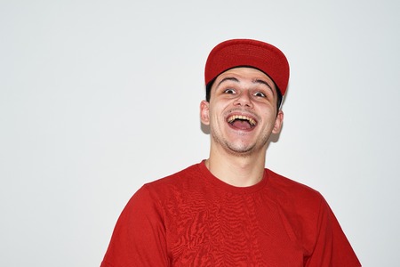 cheerful young man in a red T-shirt, baseball cap and glasses on a white backgroundの写真素材