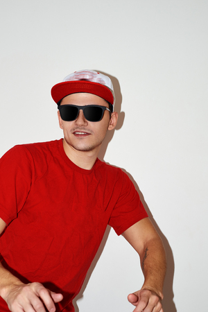 cheerful young man in a red T-shirt, baseball cap and glasses on a white backgroundの写真素材
