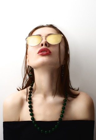 beauty girl posing on the white background with beads and bare shoulders and yellow sunglassesの写真素材