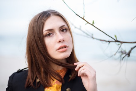stylish and fashionable young brunette girl in yellow spring color dress posing on the beach against the seaの写真素材