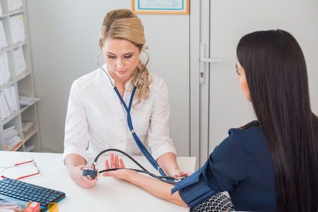 Doctor measuring pressure of the pregnant woman. Doctor taking blood pressure of female patient at officeの写真素材